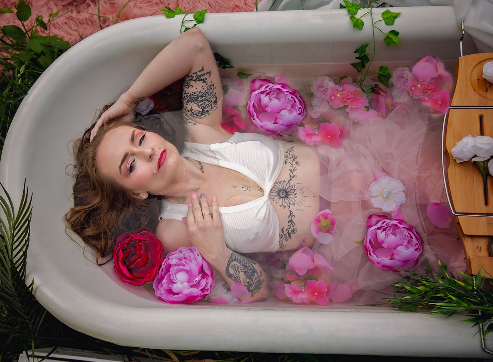 Boudoir session in vintage clawfoot tub outdoors, woman surrounded by flowers and tulle.