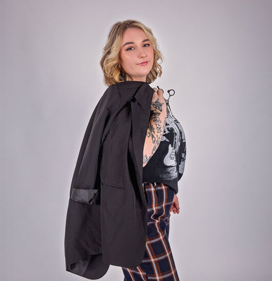 A confident young professional in a studio headshot session, with a black blazer over her shoulder, plaid pants and tattoos visible at Krystal Klear Photography, in Meaford, Ontario.