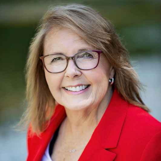 Mature woman in red blazer smiling outdoors, professional headshot – Collingwood photographer.