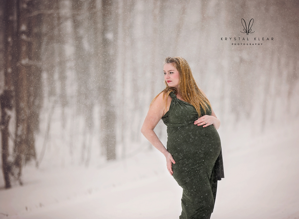 A winter maternity portrait photographed in Meaford, Ontario — a pregnant woman standing in soft snowfall, captured with calm, natural light.