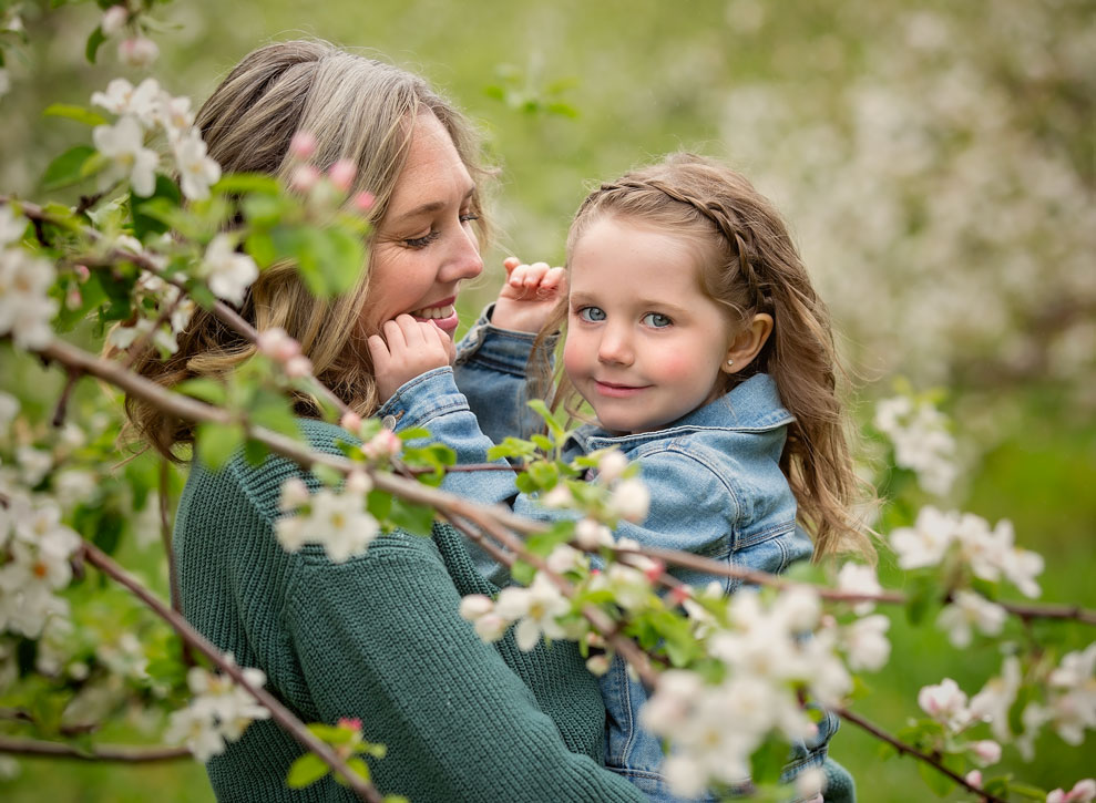 Mother holding young daughter surrounded by spring blossoms during an outdoor portrait session in Southern Georgian Bay