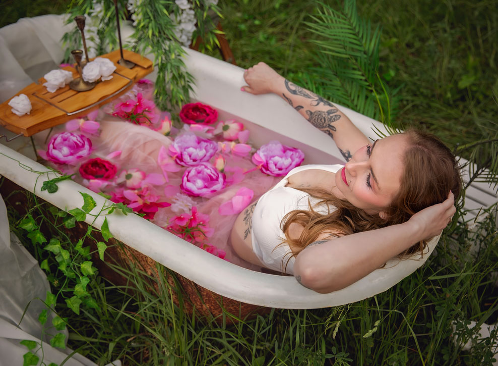 Woman relaxing in a vintage bathtub filled with pink flowers during an outdoor boudoir photography session in Southern Georgian Bay